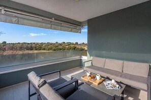 En balkon med en sofa, et bord med et fad muffins og en kop, samt et magasin.
