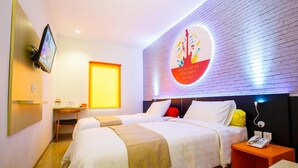Een hotelkamer met twee bedden, een aan de muur bevestigde televisie, een klein bureau en een wandlamp.