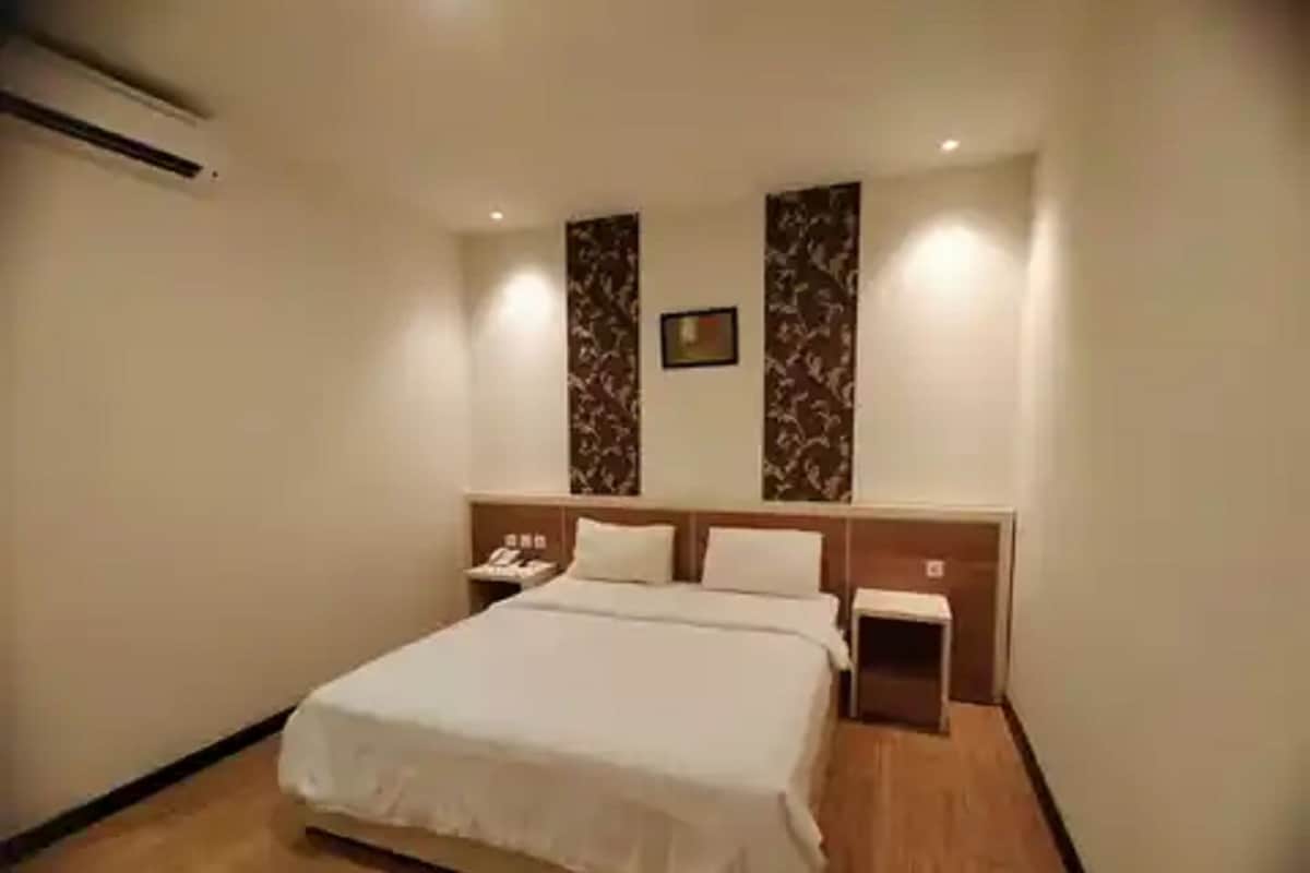A hotel room with a large bed, a bedside table, a nightstand, and a wall-mounted telephone.