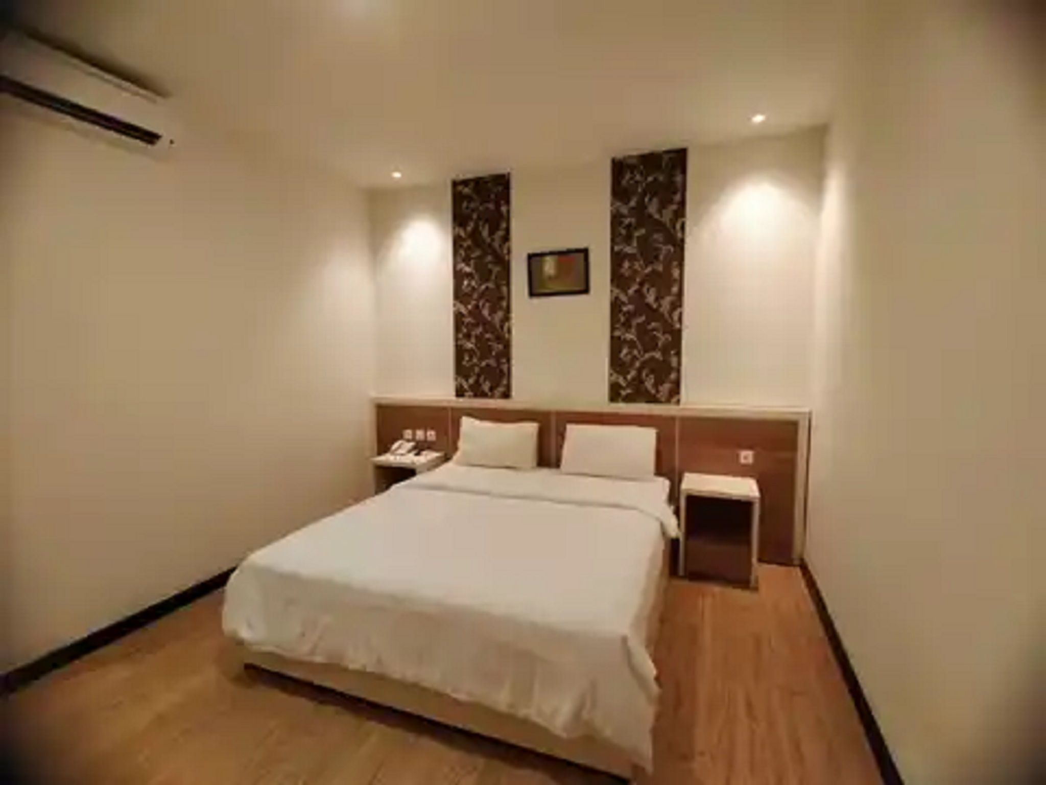 A hotel room with a large bed, a bedside table, a nightstand, and a wall-mounted telephone.