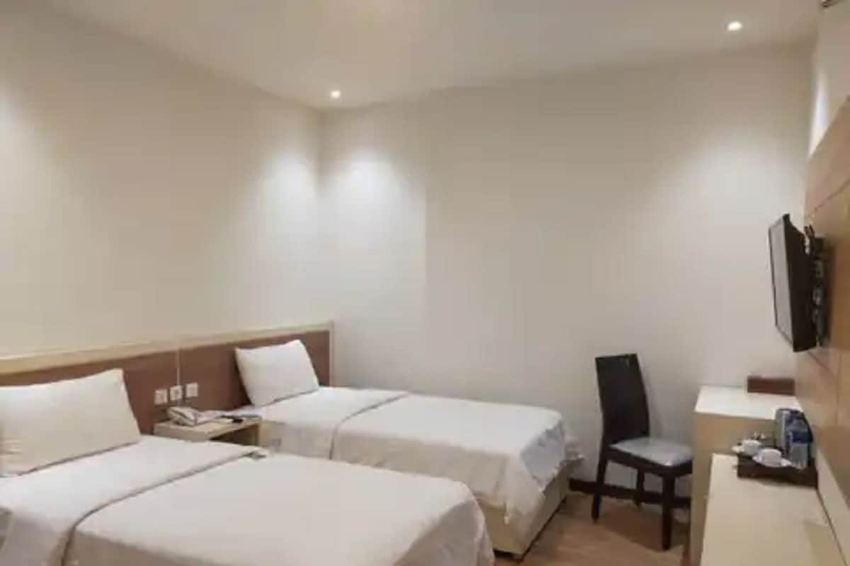 A hotel room with two beds, a desk, a chair, and a TV mounted on the wall.