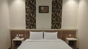 A hotel room with a large bed, two bedside tables, a nightstand, and a wall-mounted painting. - Hotel 88 Banjarmasin (Banjarmasin)