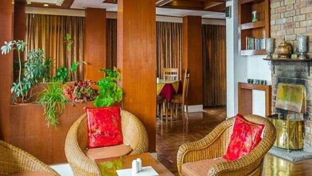 A cozy lobby with wicker furniture, a brick fireplace, and a dining area with a table and chairs. - Hotel Shangri-la Regency (Darjeeling)