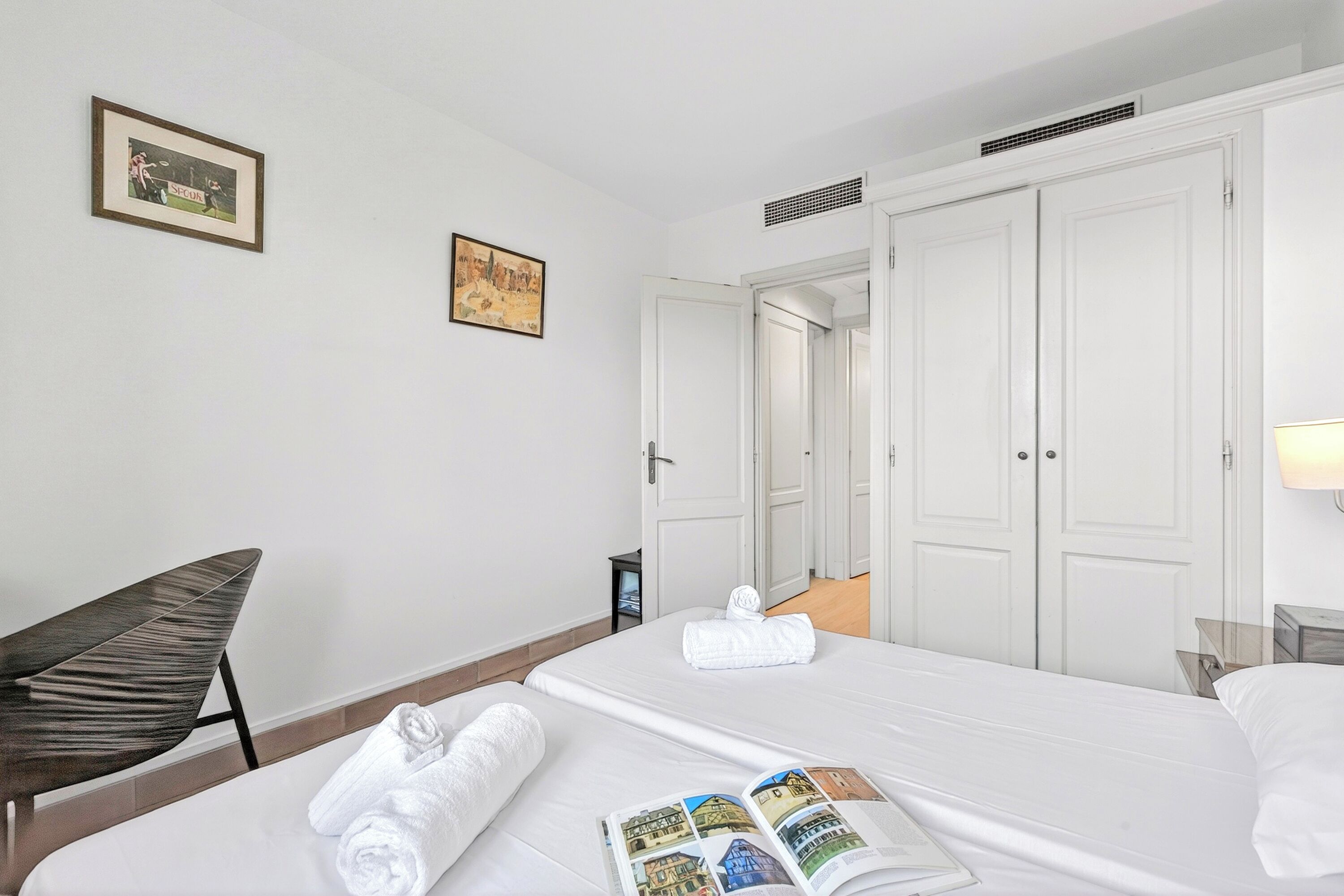 Une chambre d’hôtel avec deux lits, une chaise, un tableau encadré et une lampe.
