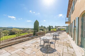 Eine Terrasse mit Sitzgelegenheiten im Freien, Steinboden und Blick auf die Landschaft.