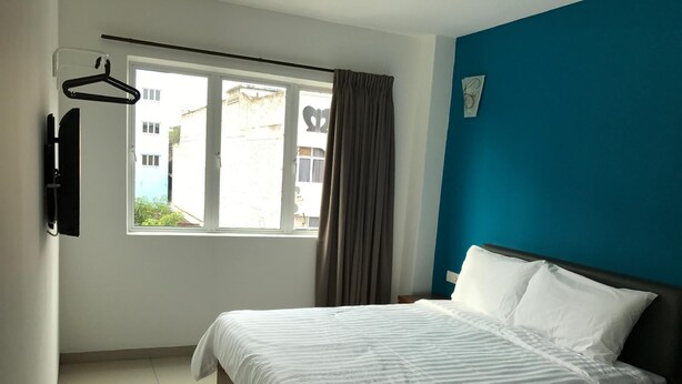 A bedroom with a bed, a window with curtains, a wall-mounted TV, and a blue accent wall. - Brezza Hotel Sitiawan (Lumut)