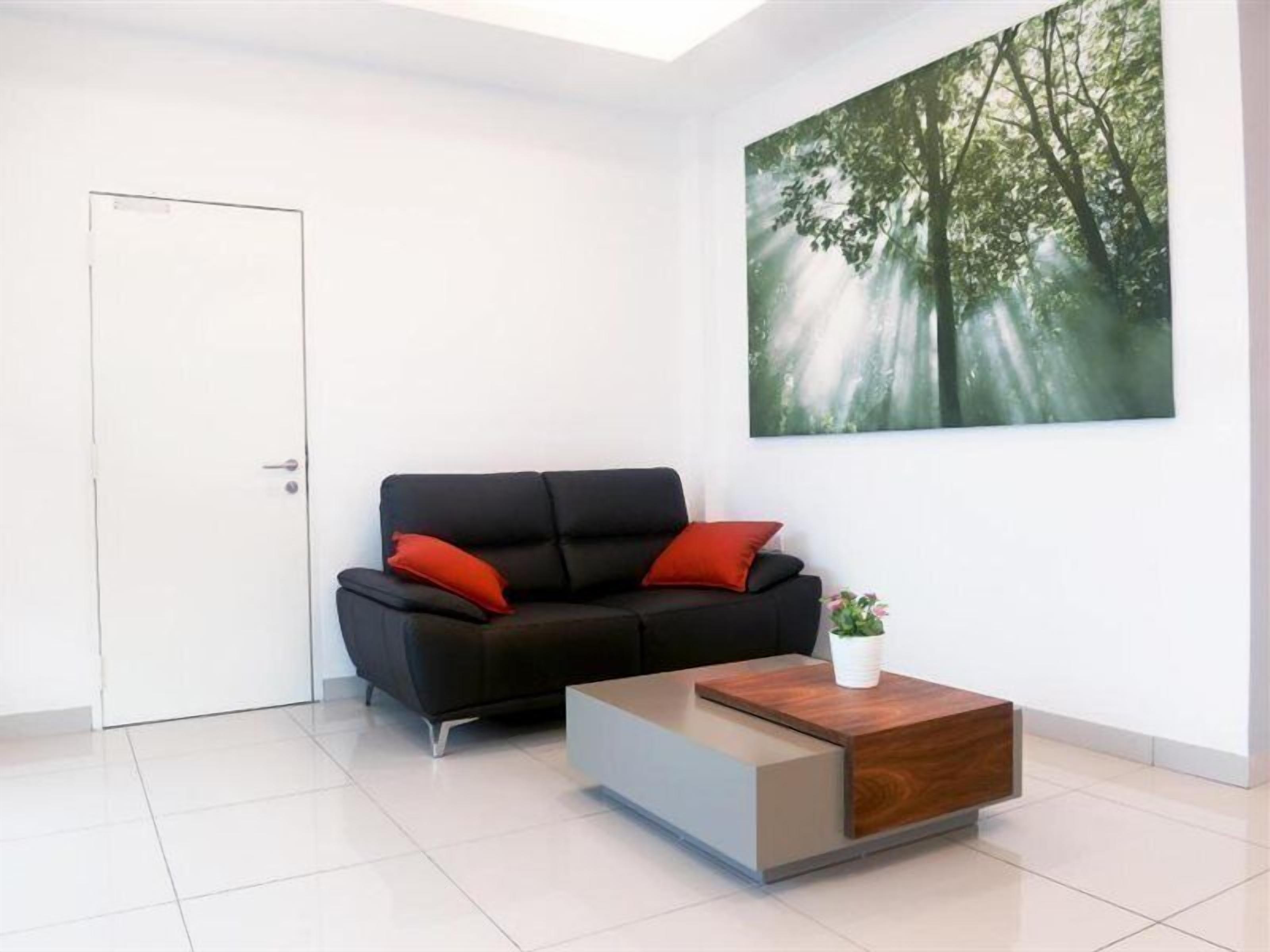 Una sala de estar moderna con un sofá negro, cojines rojos, una mesa de centro de madera y un cuadro grande con tema de bosque en la pared.