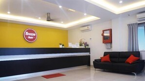A hotel reception area with a Brezza Hotel sign, a black sofa with red cushions, and a tiled floor. - Brezza Hotel Sitiawan (Lumut)