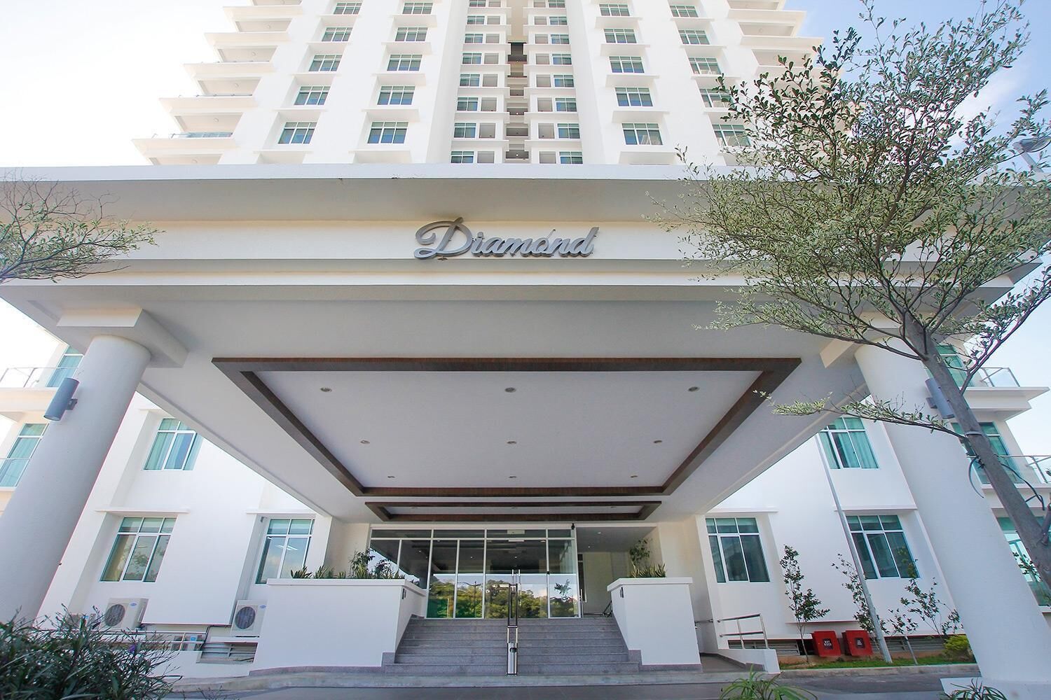 Une entrée d’hôtel moderne, dotée d’une allée couverte, de grandes fenêtres et d’une enseigne indiquant le nom « Diamond ».