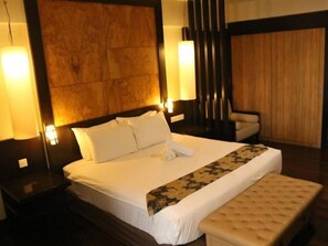 Een hotelkamer met een groot bed, een nachtkastje, een stoel en een houten hoofdeinde.