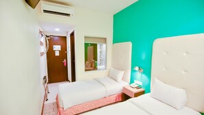 A hotel room with two beds, a green accent wall, a small bedside table with a lamp, and a door leading to another room. - Lumut Suites (Lumut)