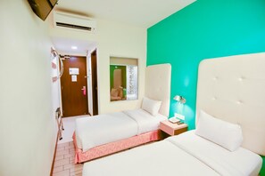 Une chambre d’hôtel avec deux lits, un mur d’accent de couleur verte, une petite table de chevet avec une lampe et une porte donnant sur une autre pièce.