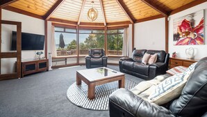 A spacious living room with a high ceiling, a large window, a leather sofa, a coffee table, and a television. - Aquarius home with vintage aesthetic and Lakeview (Rotorua)