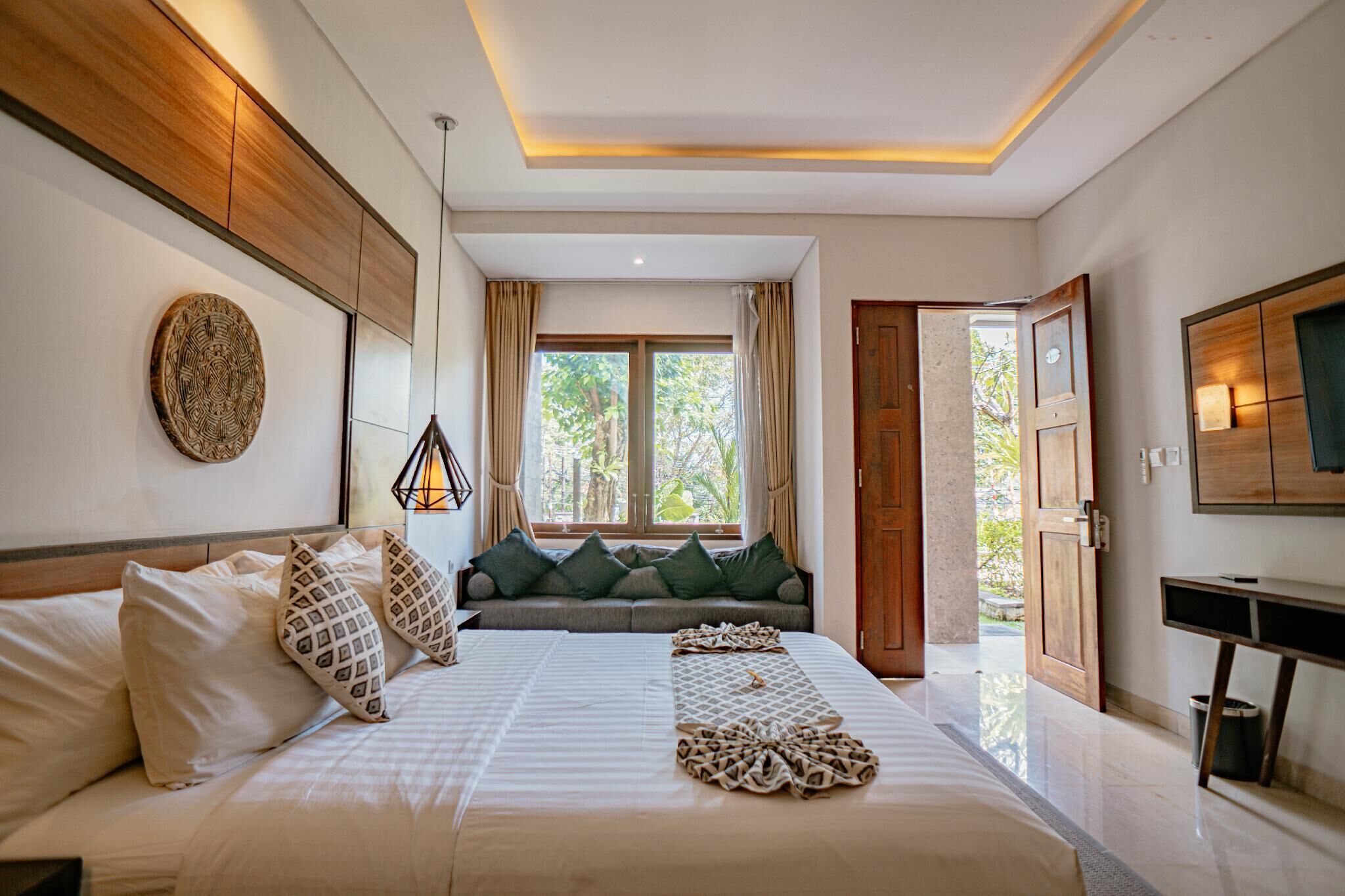 Une chambre d’hôtel moderne avec un grand lit, une tête de lit en bois, un téléviseur fixé au mur et une fenêtre avec des rideaux.