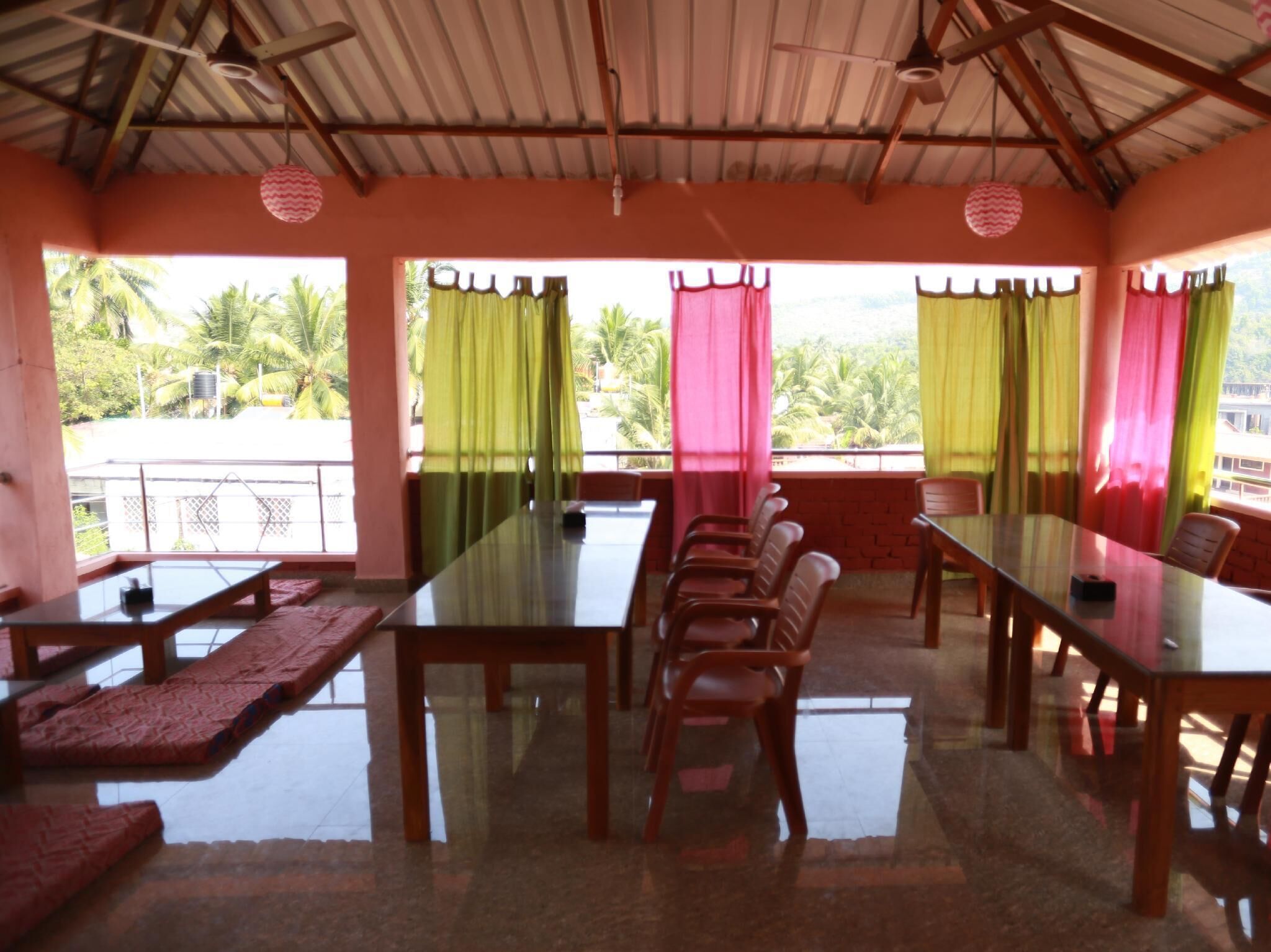 A dining area with a long table and chairs, large windows with curtains, and a view of palm trees.