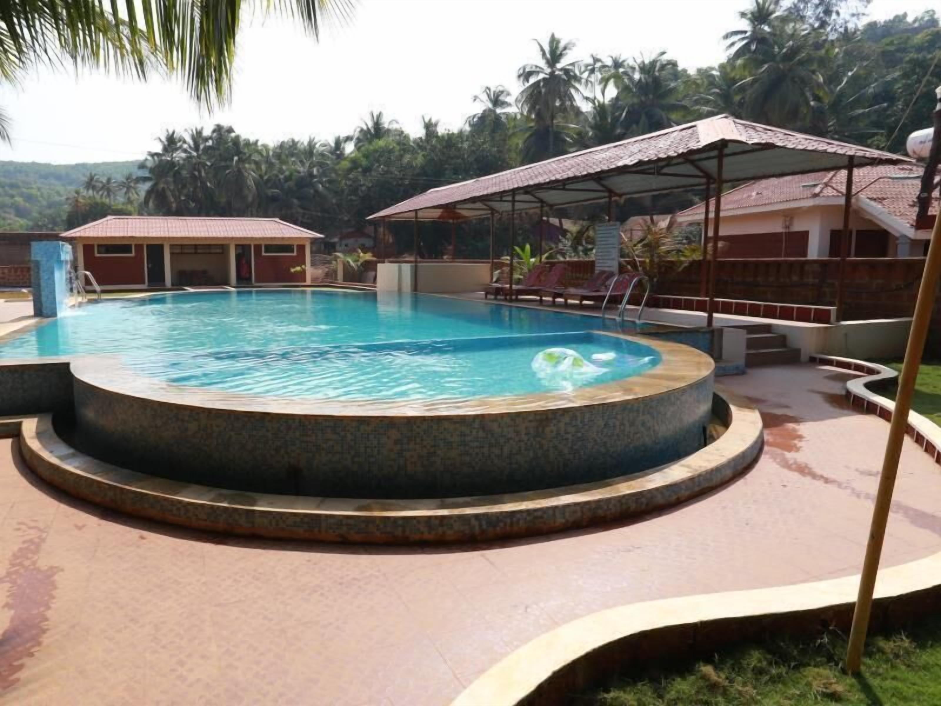 A swimming pool with a circular design, surrounded by a covered seating area and a building with a red roof.