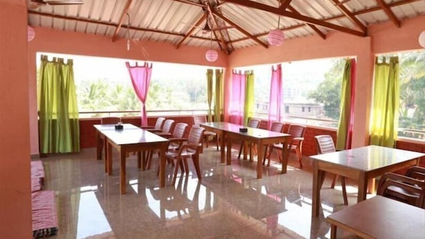 Un comedor con varias mesas y sillas, ventanas amplias con cortinas y un techo alto con vigas de madera.