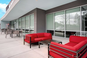 An outdoor seating area with red sofas and tables, large windows, and a modern building facade. - Avid Hotels Fort Mill - Amusement Park (Fort Mill)