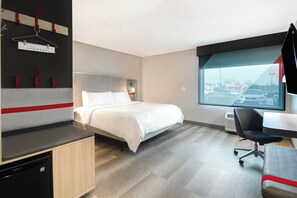Una habitación de hotel moderna con cama, escritorio y vista a un estacionamiento.