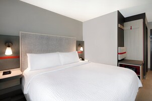 A modern hotel room with a large bed, two bedside tables with lamps, a nightstand, and a wardrobe.