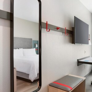 Een hotelkamer met een bed, een nachtkastje, een spiegel, een aan de muur bevestigde televisie en een bank met een rode streep.