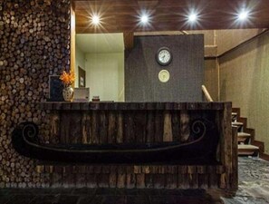 Uma área de recepção com um banco de madeira, um relógio e uma parede de troncos empilhados.