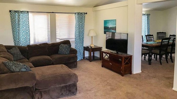 A living room with a sofa, TV, lamp, and dining area with chairs and a table.