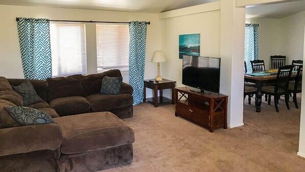 Una sala de estar con sofá, televisor, lámpara y comedor con sillas y mesa.
