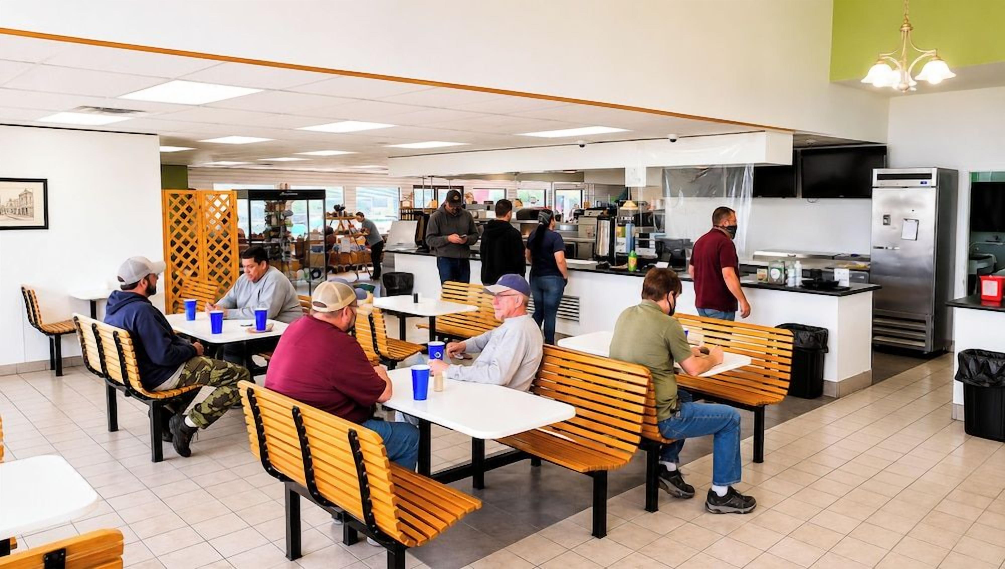 A cafeteria with tables and benches, a kitchen area, and a counter where people are ordering food.