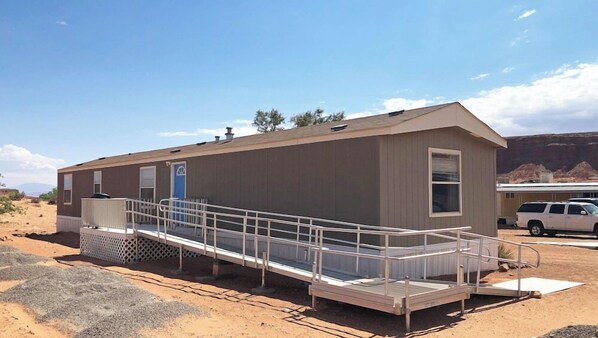A single-story mobile home with a ramp for accessibility, a small porch, and a vehicle parked nearby. - Ticaboo Lodge Lake Powell (Ticaboo)