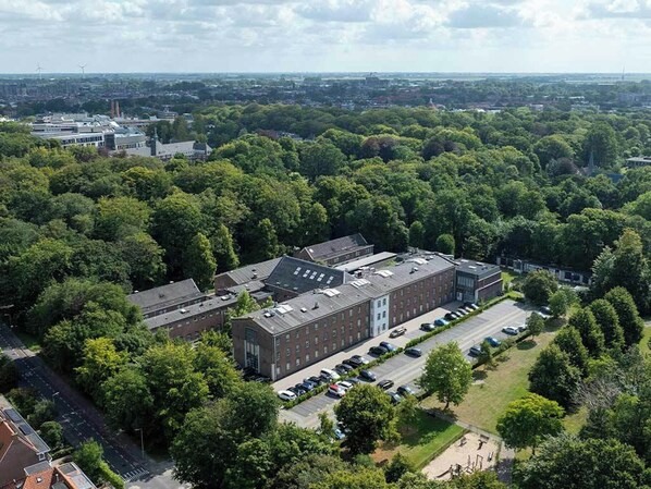 An aerial view of a campus with a large brick building surrounded by trees and a parking lot. - The Fallon Hotel Alkmaar (Alkmaar)
