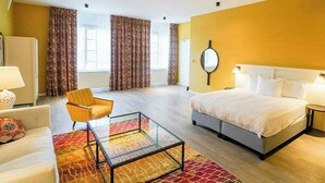 A hotel room with a bed, a chair, a glass coffee table, a sofa, and curtains. - The Fallon Hotel Alkmaar (Alkmaar)