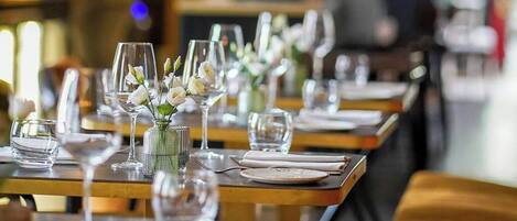 Een restaurantsetting met gedekte tafels, helder serviesglas en witte bloemen in vazen.