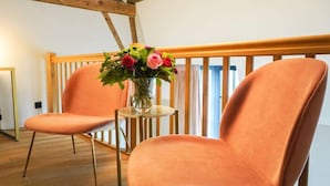 A room with two orange chairs, a small round table with a vase of flowers, and a wooden railing. - Amosa Hotel Liege & Sava Natures Cuisine (Liege)