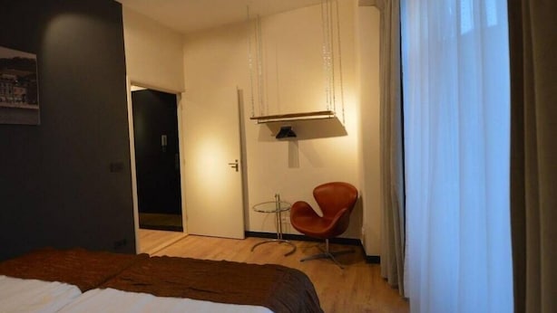 A hotel room with a bed, a chair, a small table, and a hanging light fixture. - Amosa Hotel Liege & Sava Natures Cuisine (Liege)
