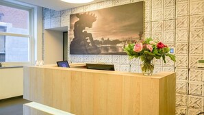 A reception desk with a tablet, a vase of flowers, and a cityscape painting on the wall. - Amosa Hotel Liege & Sava Natures Cuisine (Liege)
