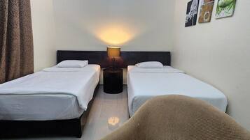 A hotel room with two single beds, a nightstand with a lamp, and a chair.