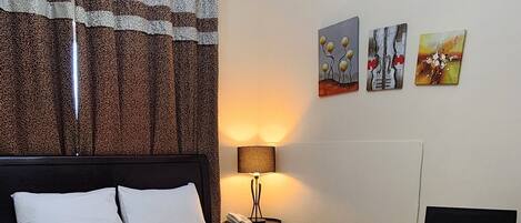 A hotel room with a bed, a bedside table, a lamp, and artwork on the wall.