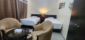 Une chambre d’hôtel avec deux lits simples, un canapé, une petite table et une lampe.