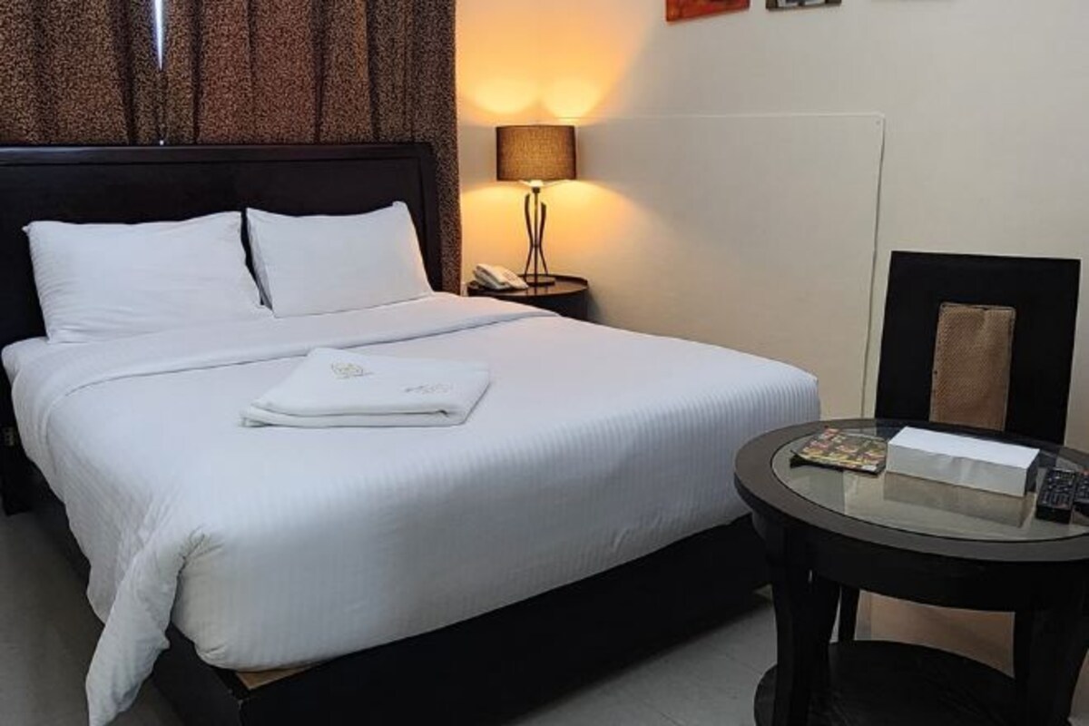 Una habitación de hotel con cama, mesita de noche, lámpara y una pequeña mesa redonda.