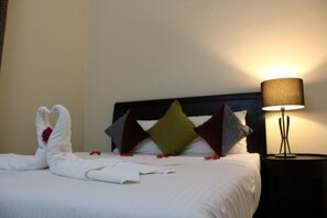 Ein ordentlich gemachtes Bett mit weißer Decke, einer dekorativen Kissenanordnung und einer Lampe auf einem Nachttisch.