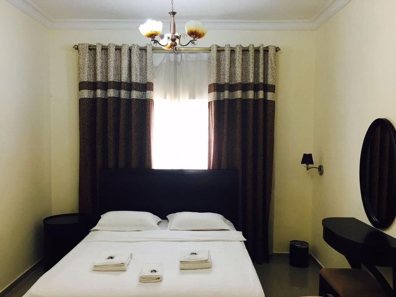 A hotel room with a bed, bedside table, lamp, and a window with curtains.