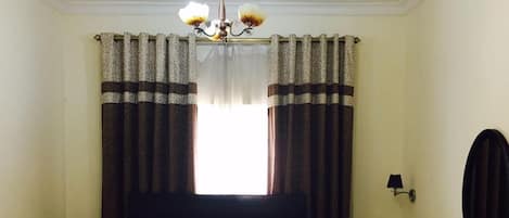A hotel room with a bed, bedside table, lamp, and a window with curtains.