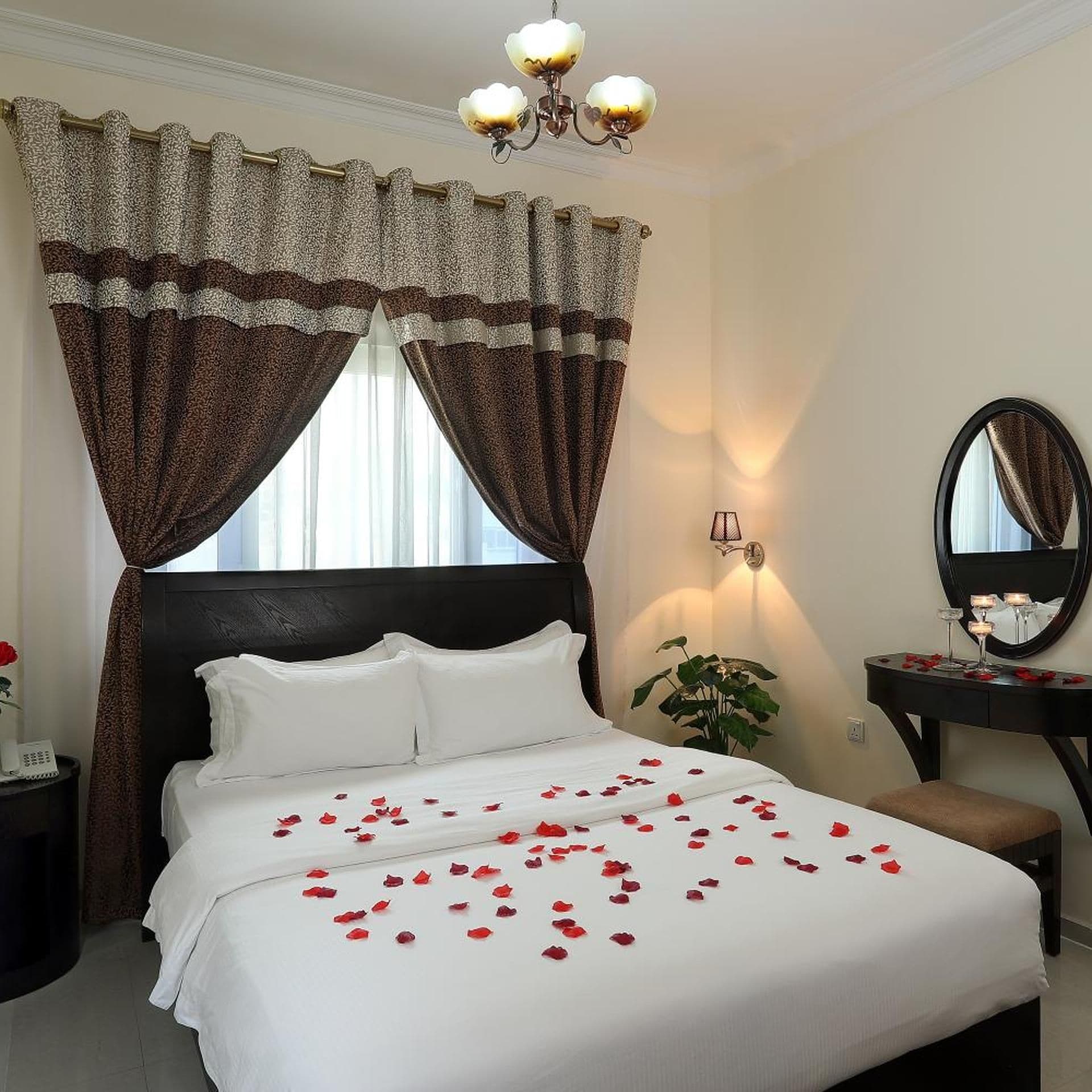A hotel room with a bed, a bedside table, a mirror, and a chandelier.