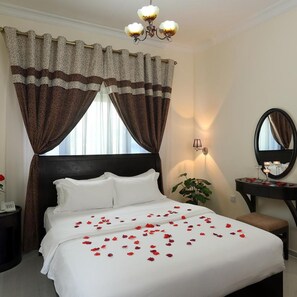 A hotel room with a bed, a bedside table, a mirror, and a chandelier. - Al Smou Hotel Apartments - Maha Hospitality Group (Ajman)