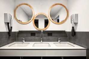 Ein modernes Badezimmer mit drei Waschbecken, drei Spiegeln und zwei Spender für Handtücher.