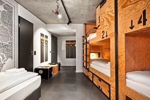 Ein Schlafraum in einer Jugendherberge mit Stockbetten, einem kleinen Schreibtisch, einem Spiegel und einer Karte an der Wand.