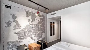 A modern hotel room with a large map mural, a neatly made bed, and a small wooden stool. - H.ostel Munster (Münster)