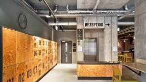A modern reception area with a wooden locker system, a reception desk, and an elevator. - H.ostel Munster (Münster)