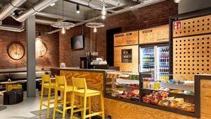 A restaurant with a brick wall, wooden bar counter, yellow chairs, and a snack display. - H.ostel Munster (Münster)